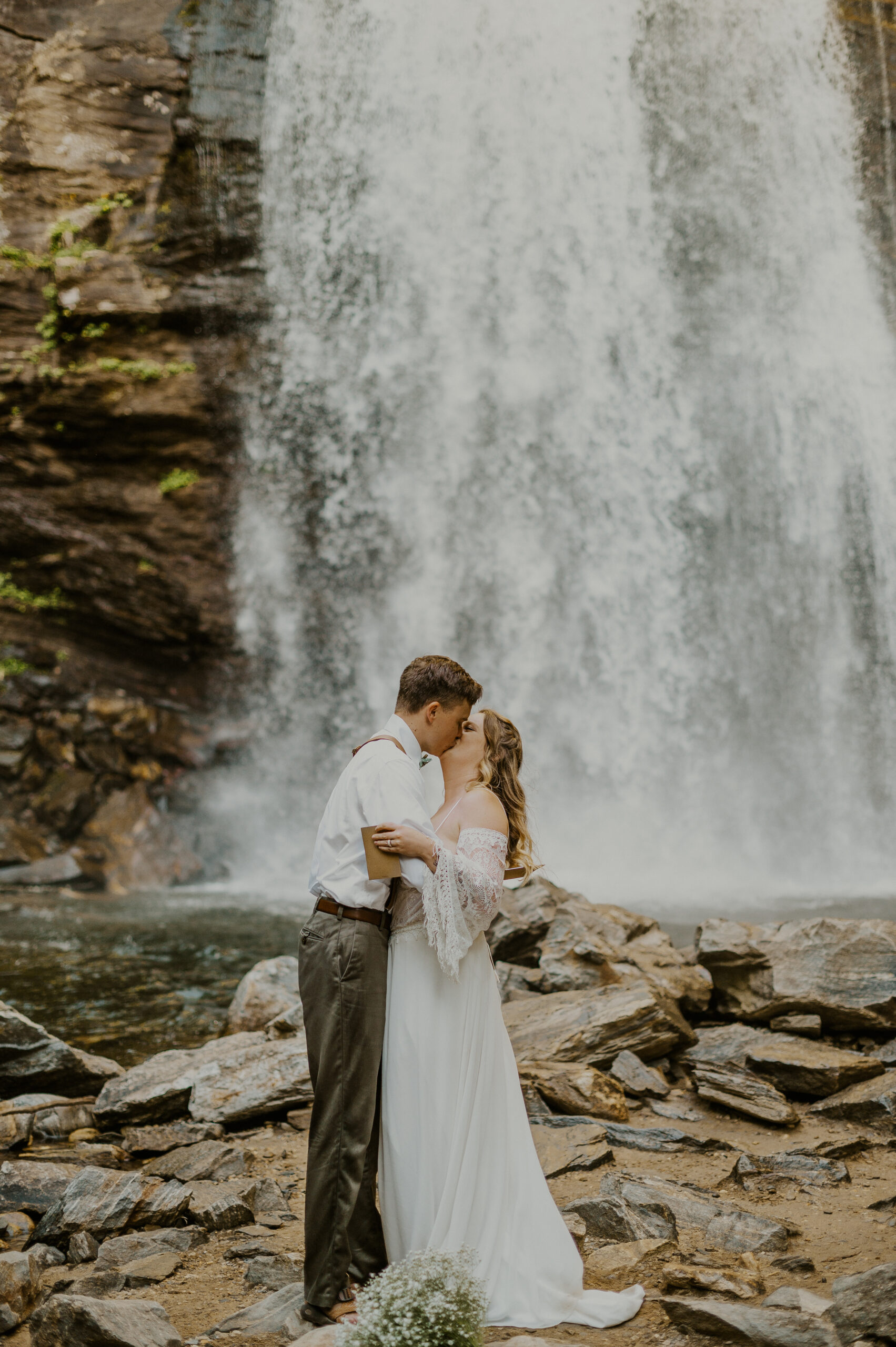 Couple kiss beneath a waterfall during their Asheville elopement ceremony.