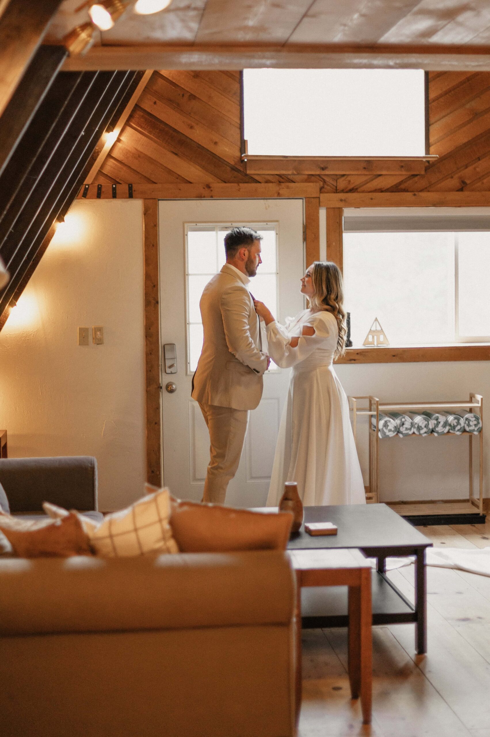 Bride helping groom with tie while getting ready in a cabin for their Colorado winter elopement. 