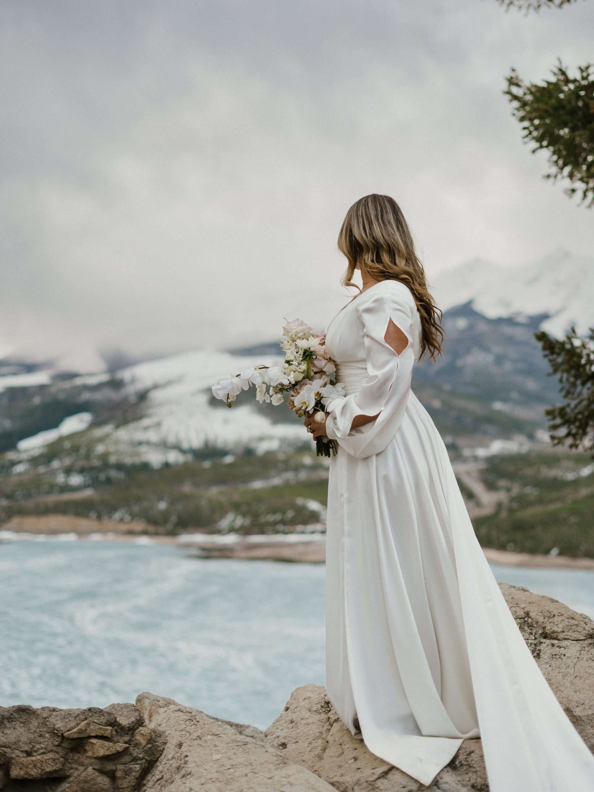 Bride looking at a frozen alpine lake in the mountains of Breckenridge during her winter elopement. 