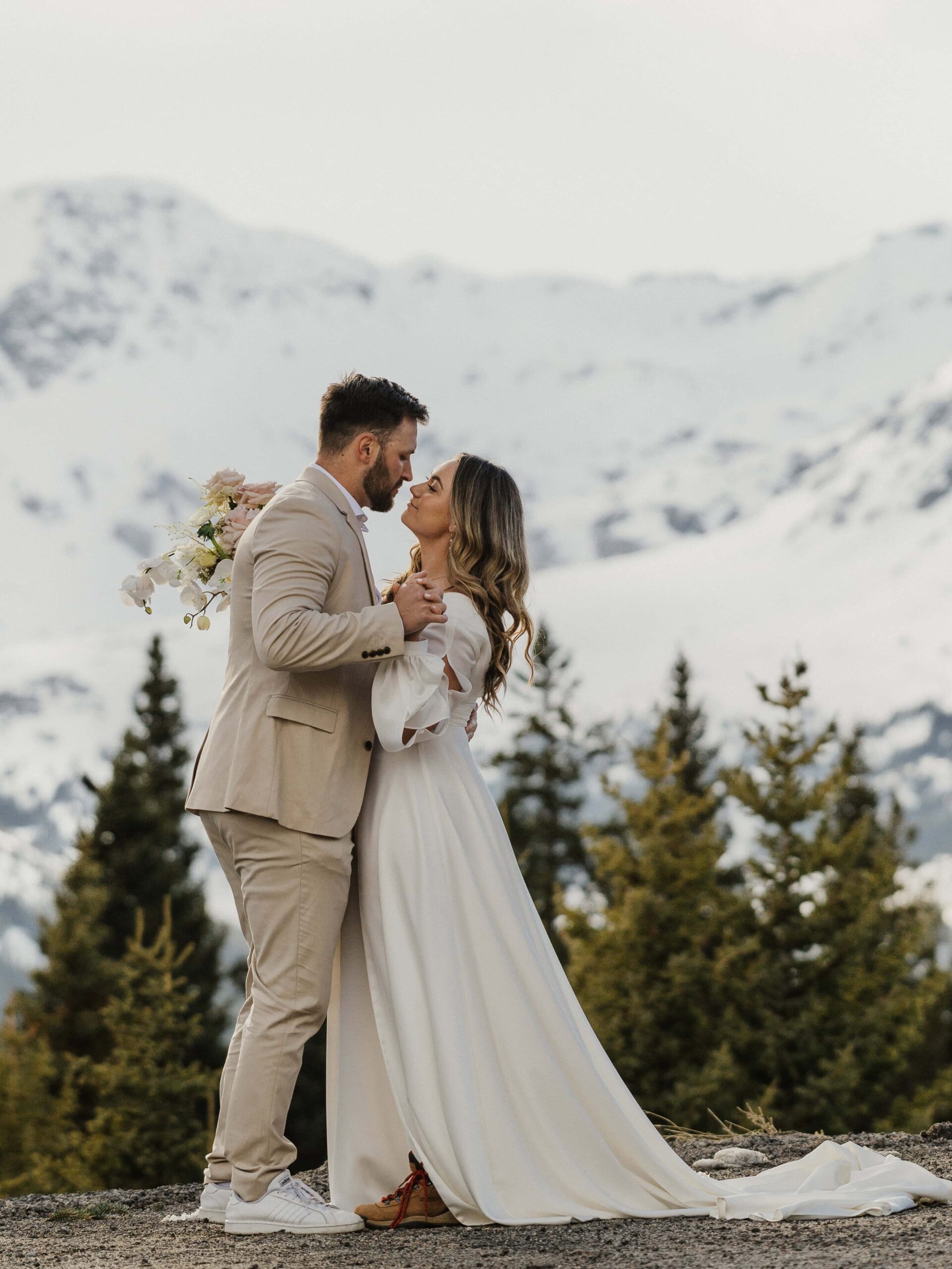 Couple holding hands & embracing in front of snow covered mountains during their luxury winter elopement in Colorado.