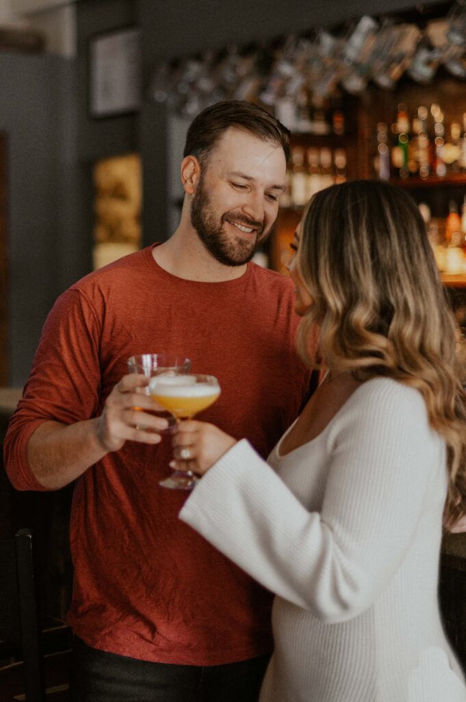 Couple smiling at each other holding drinks at a Breckenridge Brewery during the morning of their winter elopement in Colorado.