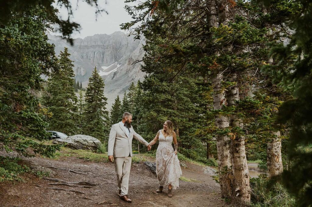 Couple holding hands walking through a pine forest after their Alta Lakes Observatory wedding ceremony.