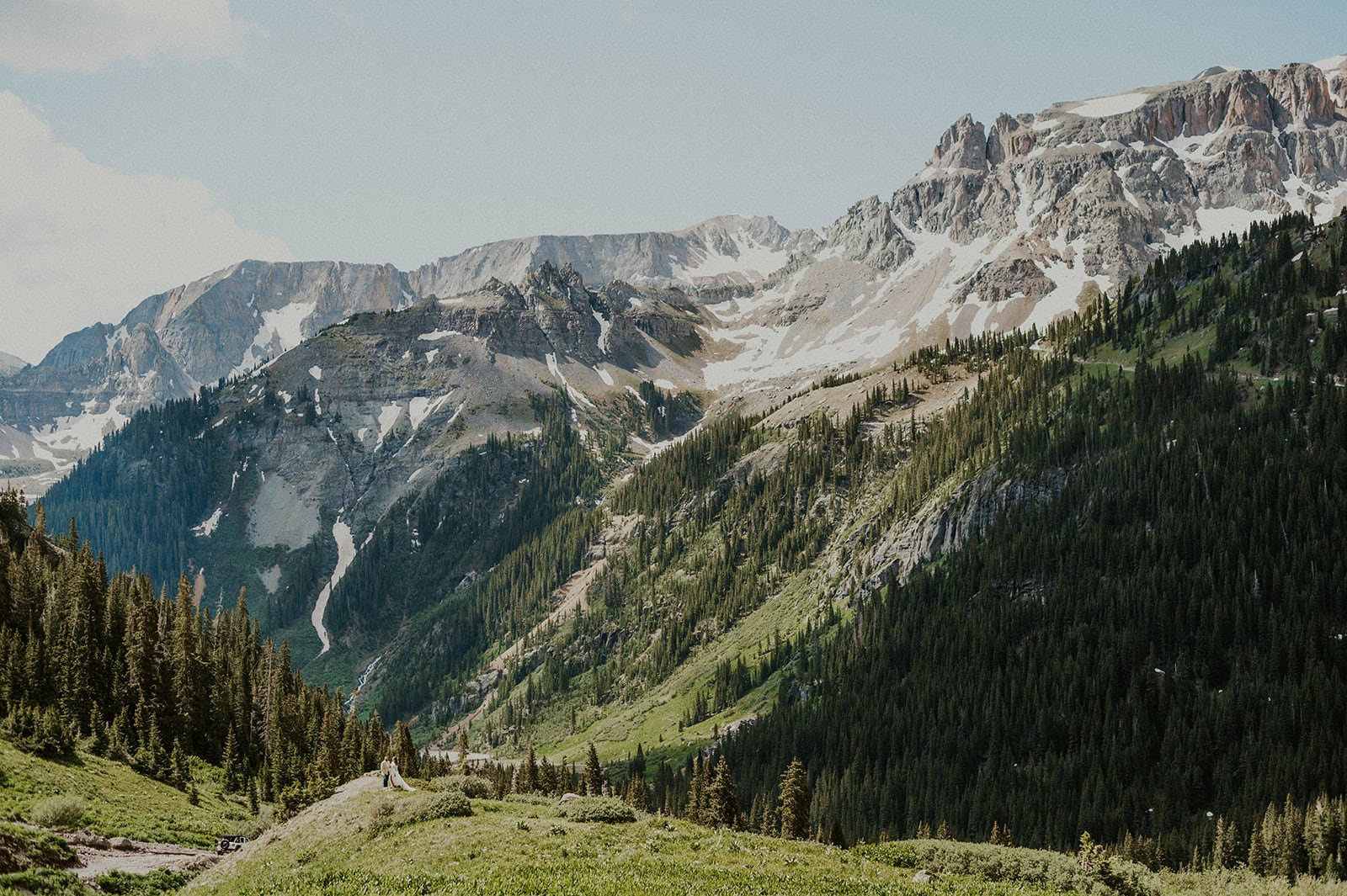 Couple standing beneath the San Juan Mountains looking small amongst the tall and rugged mountains.